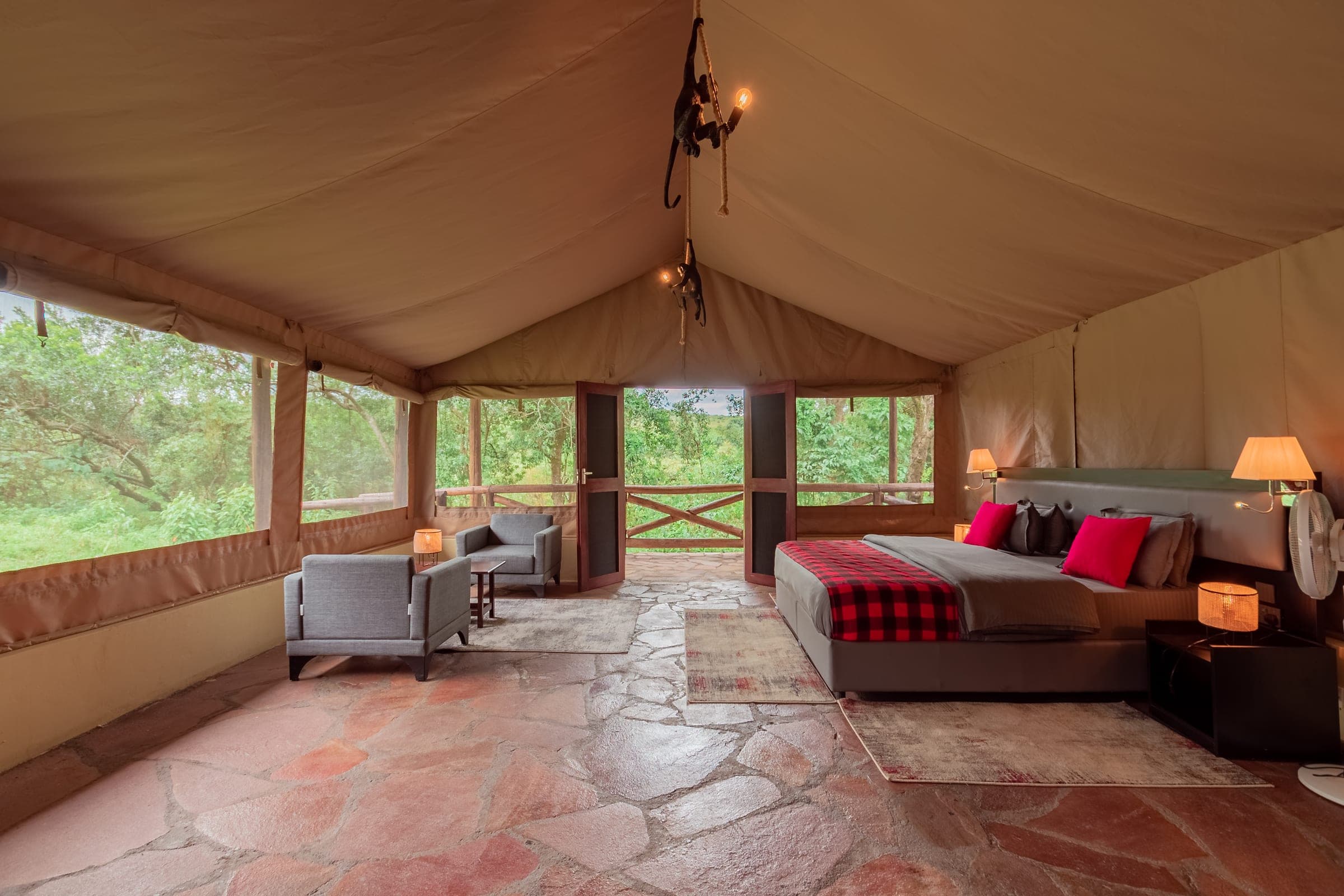 Family Tent room with a double bed in a red check throw, two armchairs and open doors to a wooden deck among trees